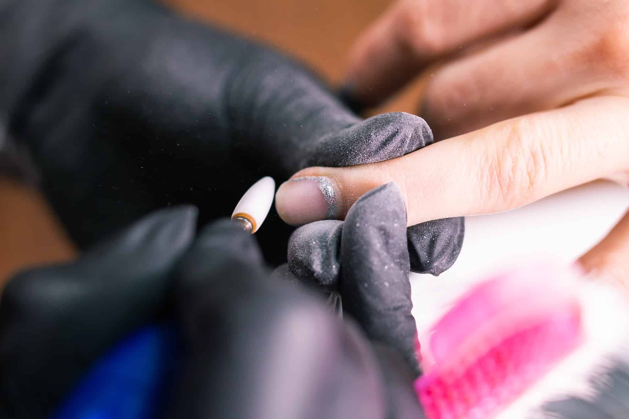 Close-up of manicurist woman removes gel shellac polish from client's nails using manicure